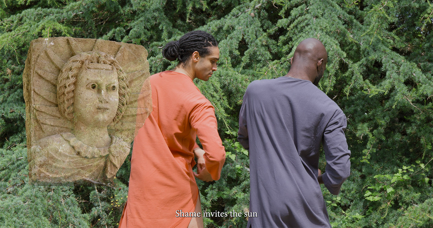 Two people are outdoors near a green cedar tree. A stone sculpture of a face is superimposed over the scene. One dancer wears orange, the other blue. The text reads: “Shame invites the sun.”