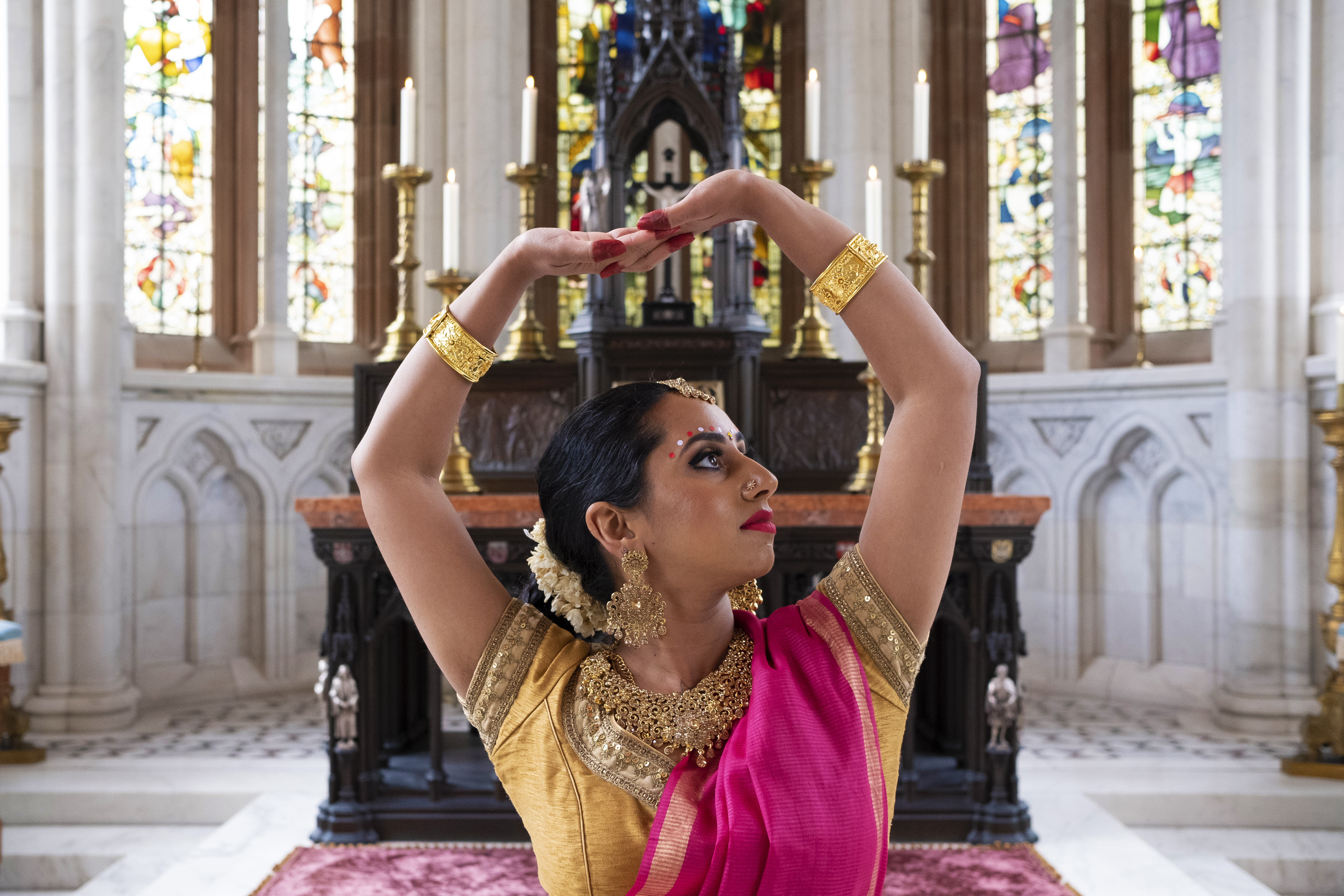 Woman wearing pink sari dancing in church with hands over head