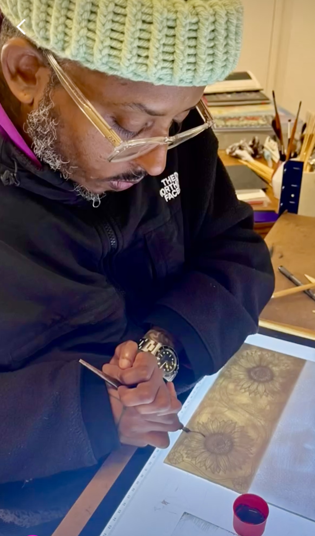 Christopher Samuel painting on a sample piece of stained glass at Studio Orme. He is drawing a sunflower.