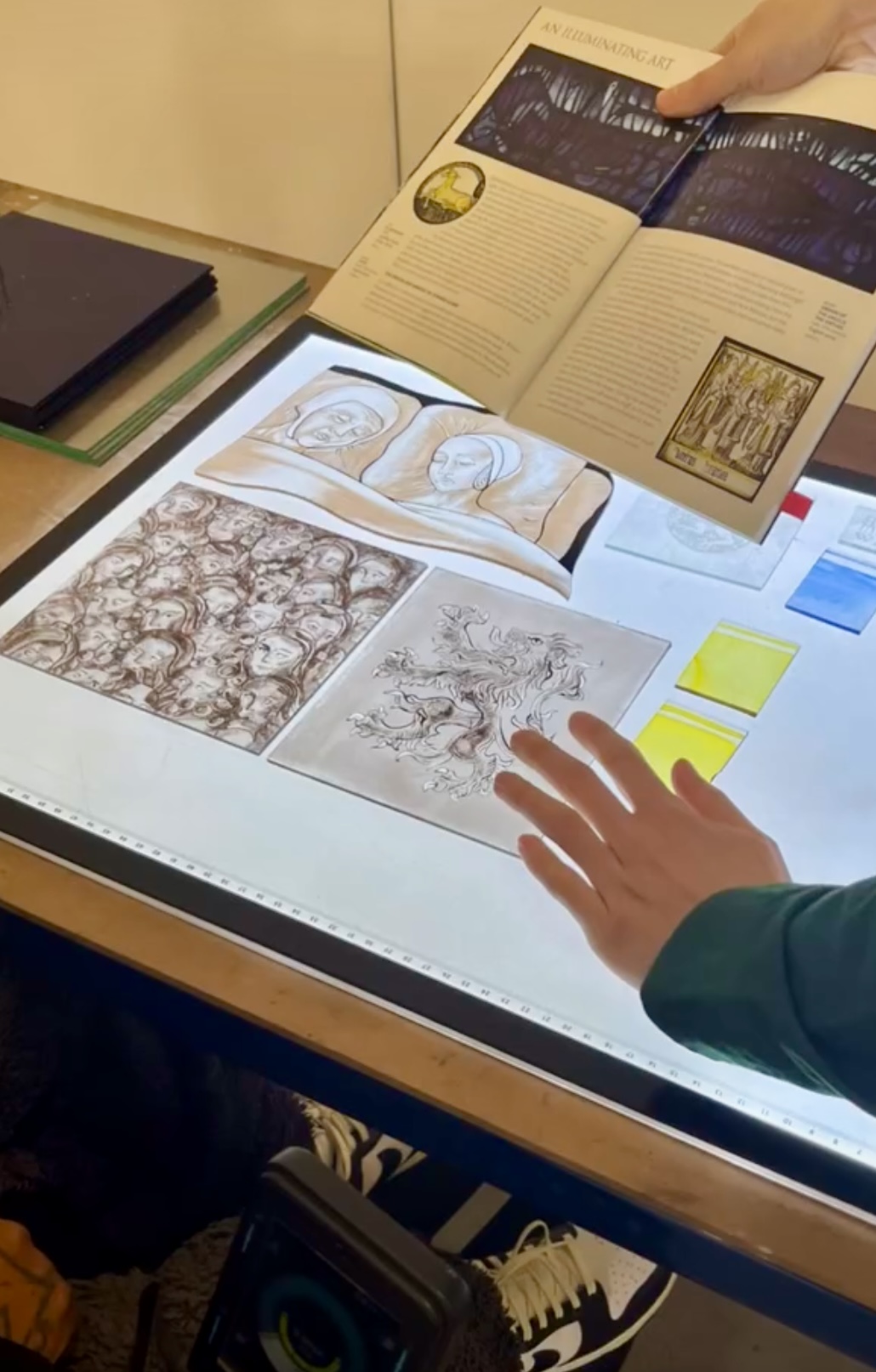 A close up of a lightbox at Studio Orme with examples of stained glass on it, and a book about stained glass techniques.