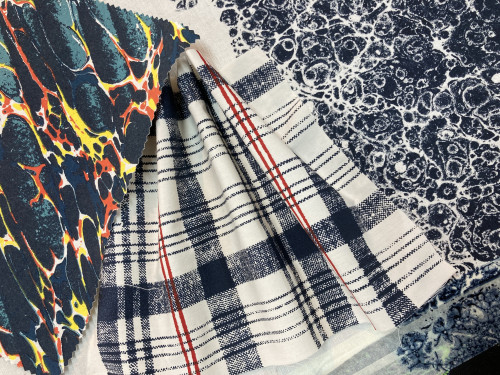 A close-up image of three overlapping fabric swatches: a navy, orange, teal and yellow marbled design, a navy and red check design, and a speckled stone-like navy design.